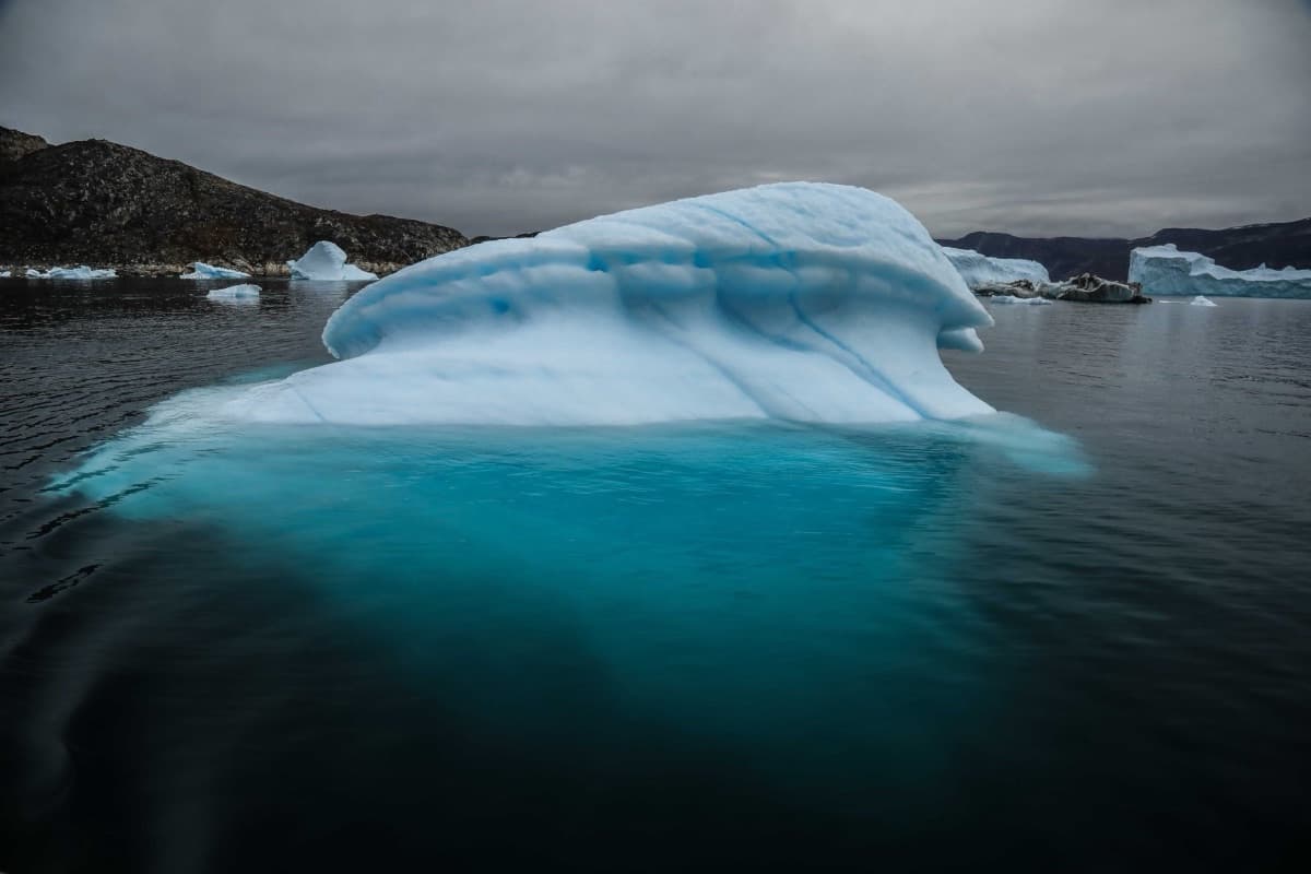 A large blue-white iceberg on dark water, its submerged base glowing turquoise beneath the surface